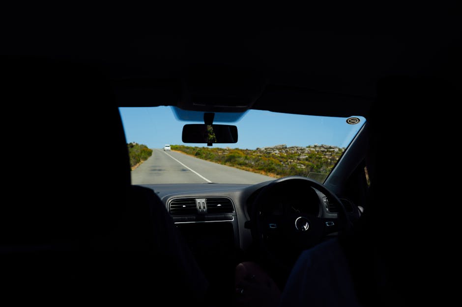View from inside a car on a scenic road, capturing a blue sky and open road ahead.